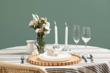 Yeşil duvarın yanında çiçekler ve yanan mumlar olan masa ayarı