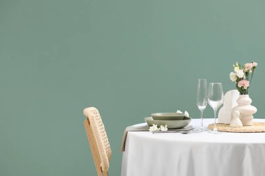 Yeşil duvarın yanında çiçekler olan güzel bir masa.