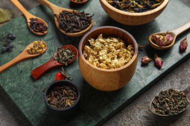 Arka planda farklı tipte kuru çay olan kaseler ve kaşıklar, yakın plan.