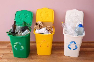 Geri dönüşüm sembollü çöp kutuları ve pembe duvarın yanındaki farklı çöpler.
