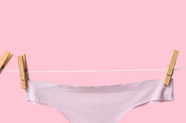 Pembe arka planda ipte sallanan kadın iç çamaşırı, yakın plan.