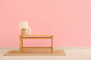 Pembe duvarın yanında lamba ve dekor olan ahşap sehpa.