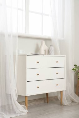 Oturma odasının penceresinin yanında vazo ve bardaklı çekmeceler.