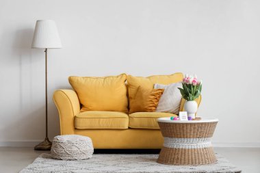 Paskalya yumurtaları, tebrik kartı ve sarı kanepenin yanındaki masada güzel lale çiçekleriyle oturma odasının içinde.