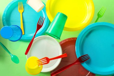 Yeşil arkaplanda renkli plastik sofra takımı yükseliyor