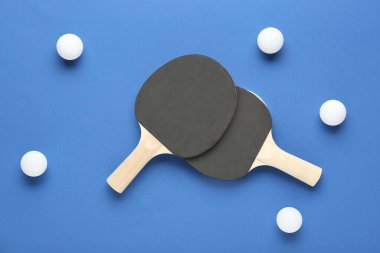 Masa tenisi raketleri ve topları mavi arkaplanda