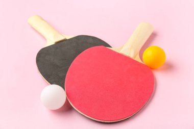 Farklı masa tenisi raketleri ve pembe arka planda toplar.