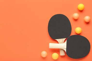 Turuncu arka planda pinpon raketleri ve topları.