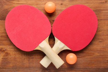 Ahşap arka planda kırmızı pinpon raketleri ve topları