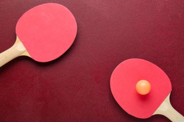 Kırmızı zemin üzerinde pinpon raketleri ve top