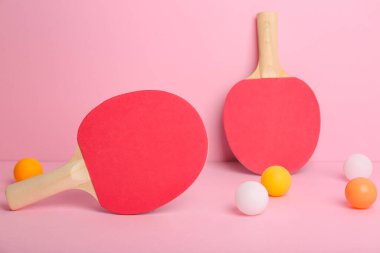 Pembe arka planda kırmızı pinpon raketleri ve topları.