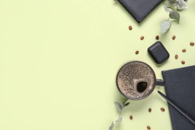 Açık yeşil arkaplan üzerinde notlar, kulaklıklar, fasulyeler ve okaliptüs dalları olan bir fincan kahve.