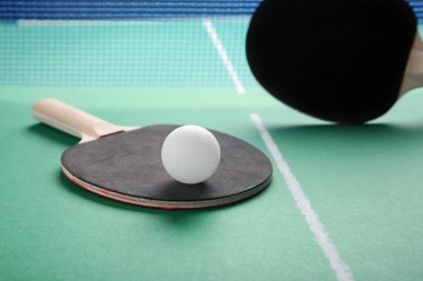 Masa tenisi raketleri ve top yeşil masada.