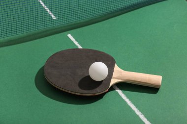 Masa tenisi raketi ve top yeşil masada ağın yanında.