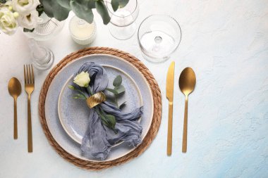 Peçete, östoma çiçeği, okaliptüs dalı ve açık mavi arkaplanda mumlarla düğün masası.