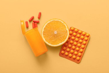 C vitamini hapları ve bej arka planda turuncu dilimli bir şişe.