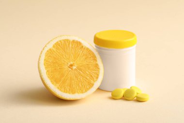 C vitamini haplı bir şişe ve sarı arka planda yarım limon.