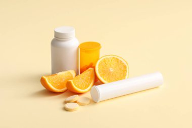 C vitamini hapları ve sarı arka planda portakal dilimleri olan şişeler.