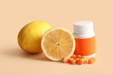 C vitamini hapları ve bej arka planda limonlarla dolu bir şişe.