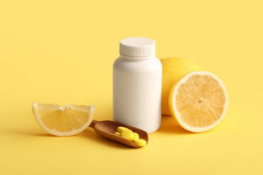C vitamini hapları, ahşap kepçe ve sarı arka planda limon dilimleri.