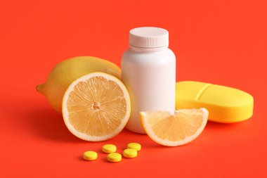 C vitamini hapları, limon dilimleri ve kırmızı arka planda plastik düzenleyici.