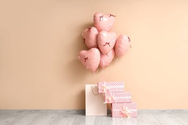 İçinde kalp şeklinde balonlar ve bej duvarın yanında hediye kutuları olan alışveriş torbası. Sevgililer Günü kutlaması