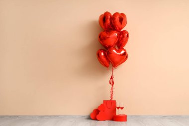 İçinde kalp şeklinde balonlar, hediye kutuları ve bej duvarın yanında şarap bardakları olan bir alışveriş çantası. Sevgililer Günü kutlaması