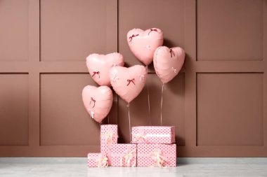 Kahverengi duvarın yanında kalp şeklinde balonlar olan hediye kutuları. Sevgililer Günü kutlaması