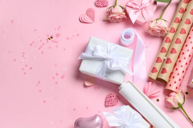 Kurdeleli hediye kutuları, kalpler, gül çiçekleri ve pembe arka planda ambalaj kağıtları. Sevgililer Günü kutlaması