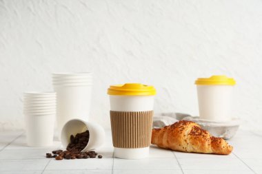 Kahve çekirdekli kağıt bardaklar ve fayans masasında beyaz arka planda kruvasan.