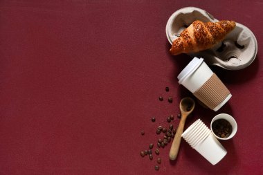 Kahve çekirdekli kağıt bardaklar ve kırmızı arka planda kruvasan.