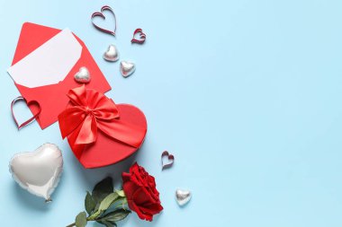 İçinde kağıt kalpler, şekerler, zarf, boş kart ve mavi arka planda gül çiçeği olan hediye kutusu. Sevgililer Günü kutlaması