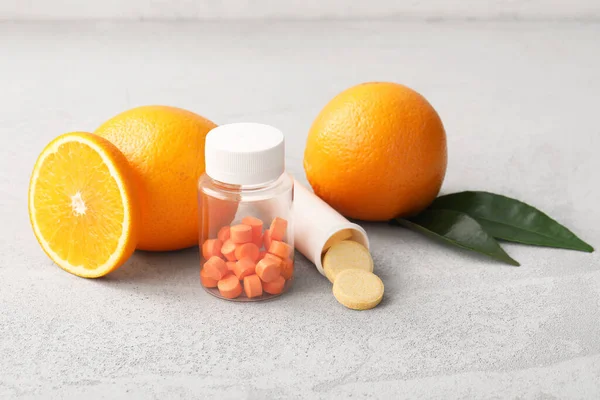 C vitamini haplı şişeler ve gri grunge arka planda portakallar.