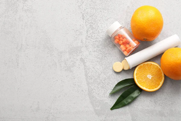 C vitamini haplı şişeler ve gri grunge arka planda portakallar.