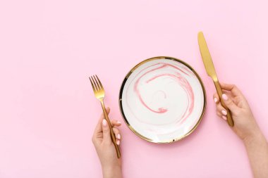 Çatal bıçaklı ve pembe arka planda boş tabağı olan kadın.