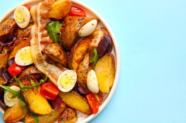 Yumurtalı, domatesli ve açık mavi arka planda domuz pastırmalı lezzetli patates salatası.