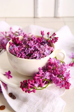 Aydınlık masada bir fincan güzel leylak çiçekli kompozisyon, yakın plan.