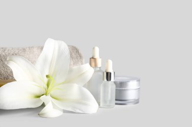 Kozmetik ürünler seti, temiz havlu ve gri arka planda güzel zambak çiçeği.