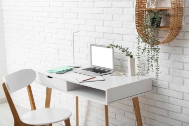 Beyaz duvarın yanında dizüstü bilgisayarı ve sandalyesi olan şık bir iş yeri.