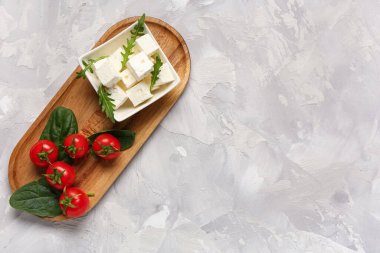 Gri arkaplanda beyaz peynir, roka ve vişneli domateslerle dolu bir kase.