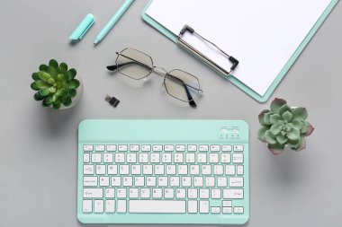 Gri arka planda klavye, gözlük ve kaktüs. Üst görünüm