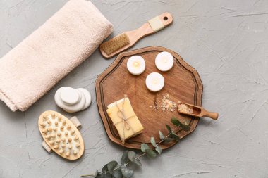 Sabun çubukları, mumlar, okaliptüs dalı ve gri arka planda bir kepçe deniz tuzu olan ahşap tepsi.