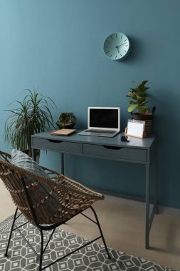 Ofiste mavi duvarın yanında dizüstü bilgisayarı ve bitkileri olan modern bir işyeri.