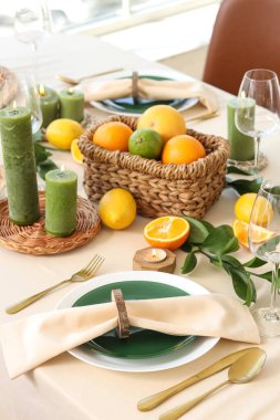 Oturma odasında turunçgil meyveleri, yanan mumlar ve beyaz masa örtüsü olan güzel bir masa.