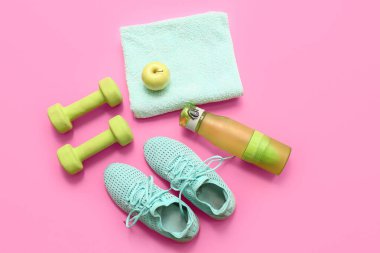 Spor ayakkabıları, havlu, dambıllar, spor su şişesi ve pembe arka planda elma.
