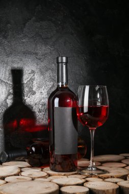 Siyah grunge arka planına karşı ahşap masada şişe ve bir bardak kırmızı şarap.