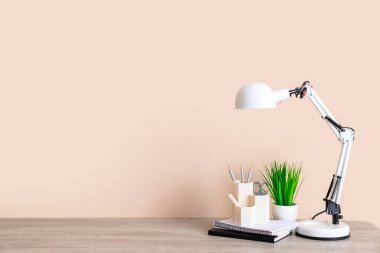 Oda içinde bej duvar yakınında masa lambası, ev bitkisi ve ofis malzemesi olan modern işyeri