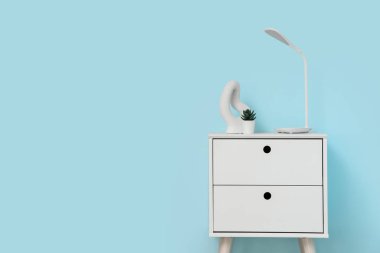 Masa lambası, çiçek ve biblo mavi duvarın yanındaki odada.