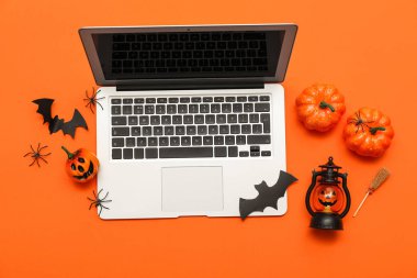 Turuncu arka planda Cadılar Bayramı için modern dizüstü bilgisayar ve dekor kompozisyonu