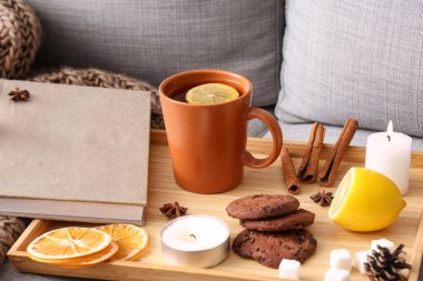 Limon çaylı tepsi, kurabiyeler, yanan mumlar ve kanepede kitap, yakın plan.